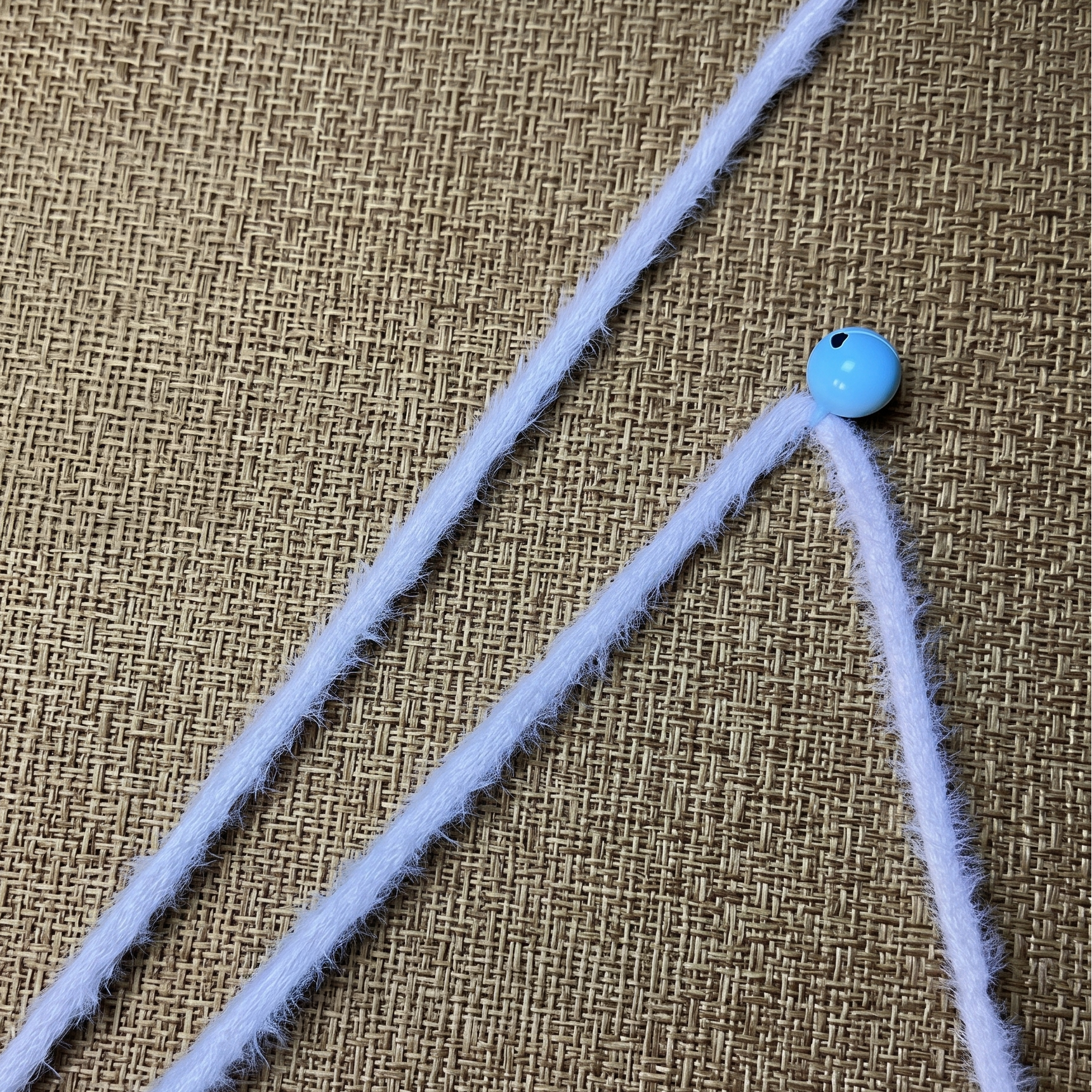 Close-up of the white, plush fleece-wrapped handle and small blue bell on the premium cat teaser wand.