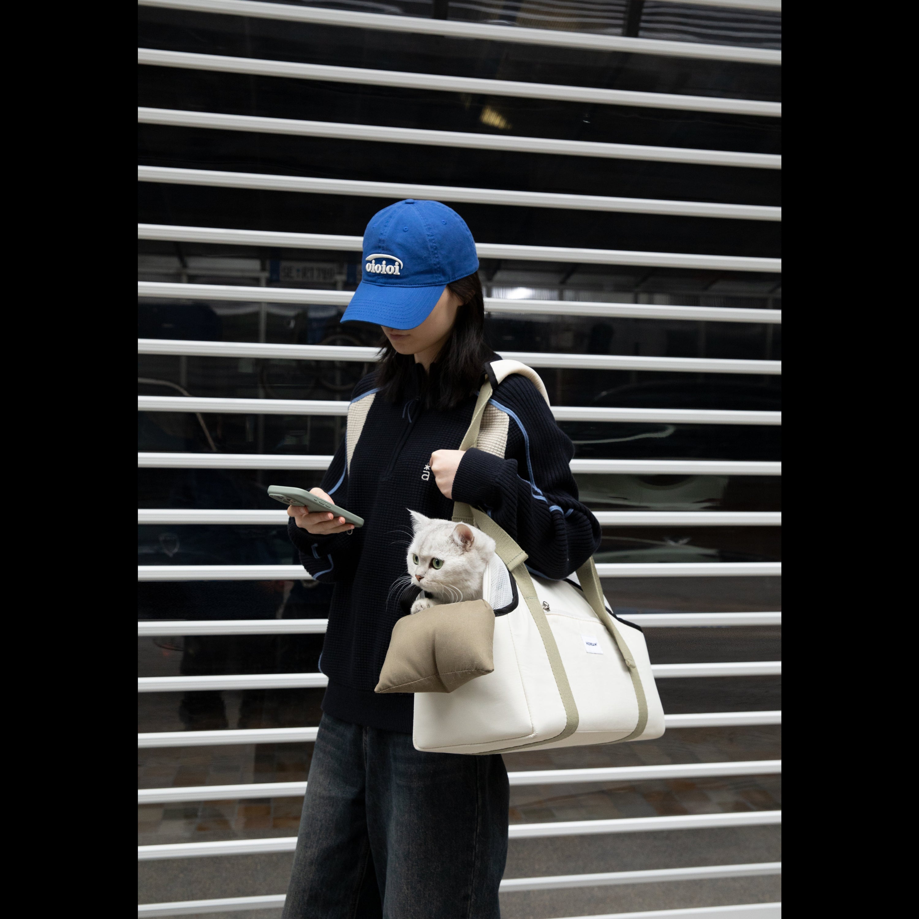 A pet owner carrying the canvas-style cat tote bag on her shoulder. A silver cat is safely looking out from the U-shaped opening while resting on the built-in chin pad.