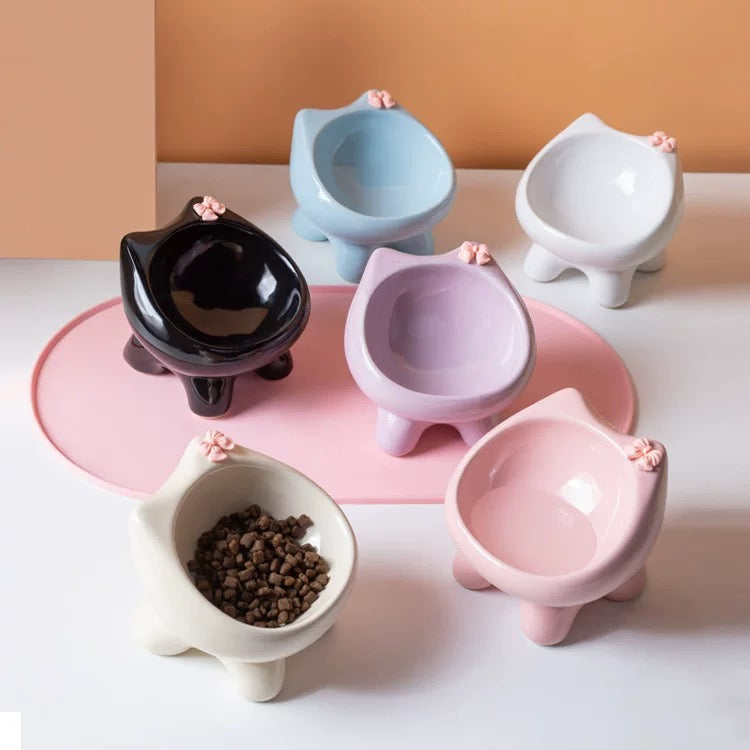 A collection of five adorable cat-ear ceramic bowls in black, blue, white, purple, and pink, displayed on a pink mat to showcase the stylish elevated design.