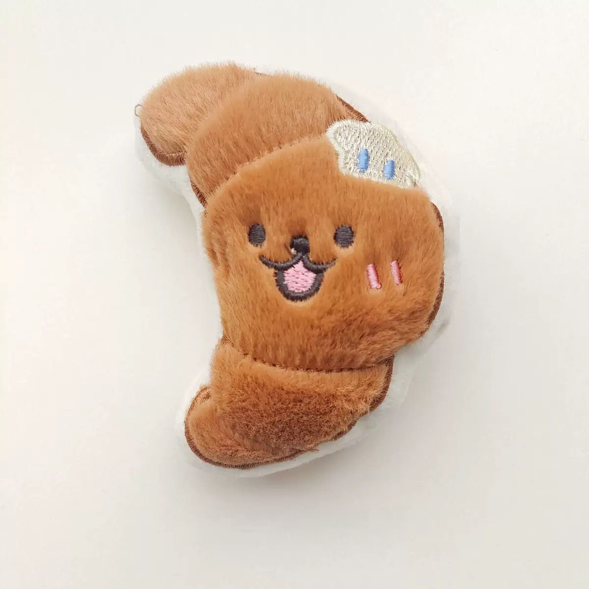 A petite 9.5cm flaky croissant plush toy with a soft brown texture and a tiny butter embroidery on the side.