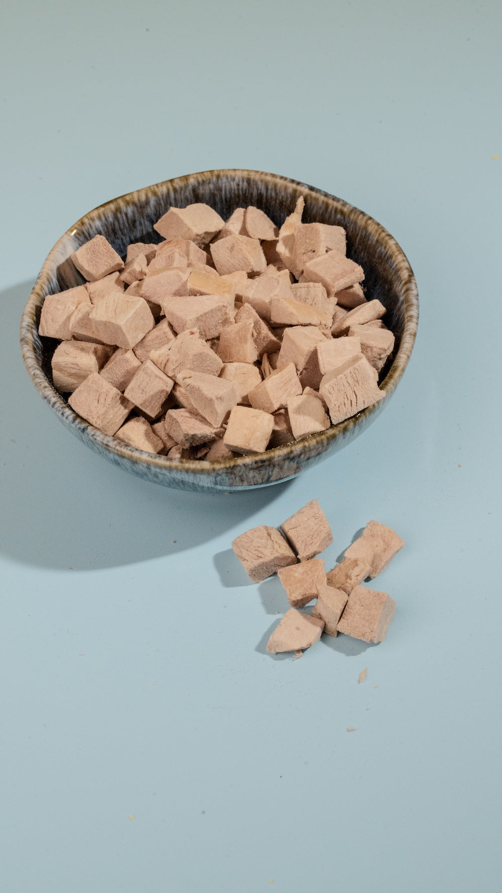 Bowl of freeze-dried duck cubes c on a light blue background