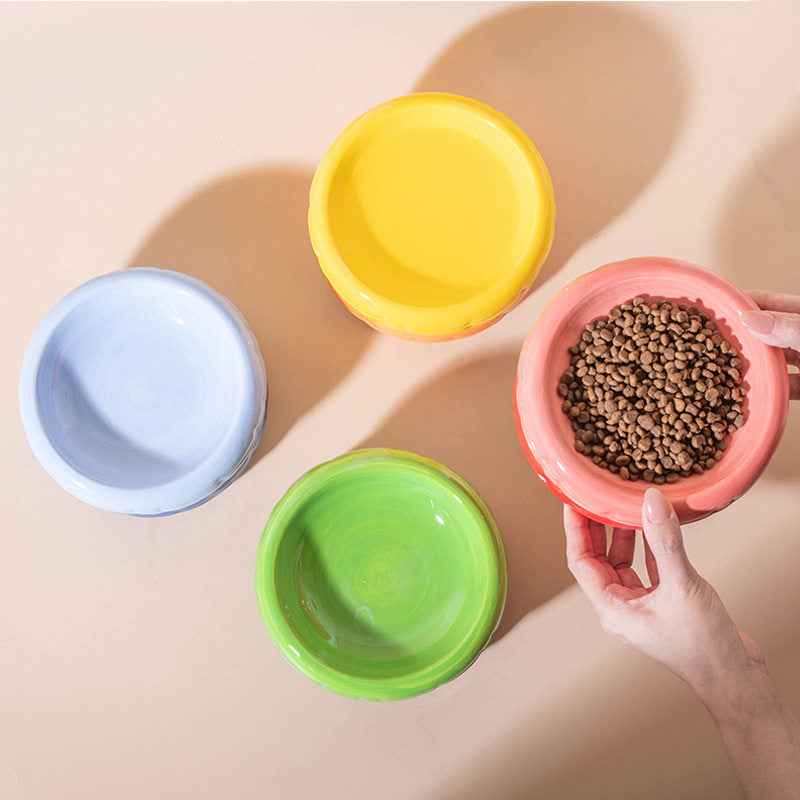 An overhead view of four ceramic cat bowls in light blue, yellow, green, and pink, with a person&