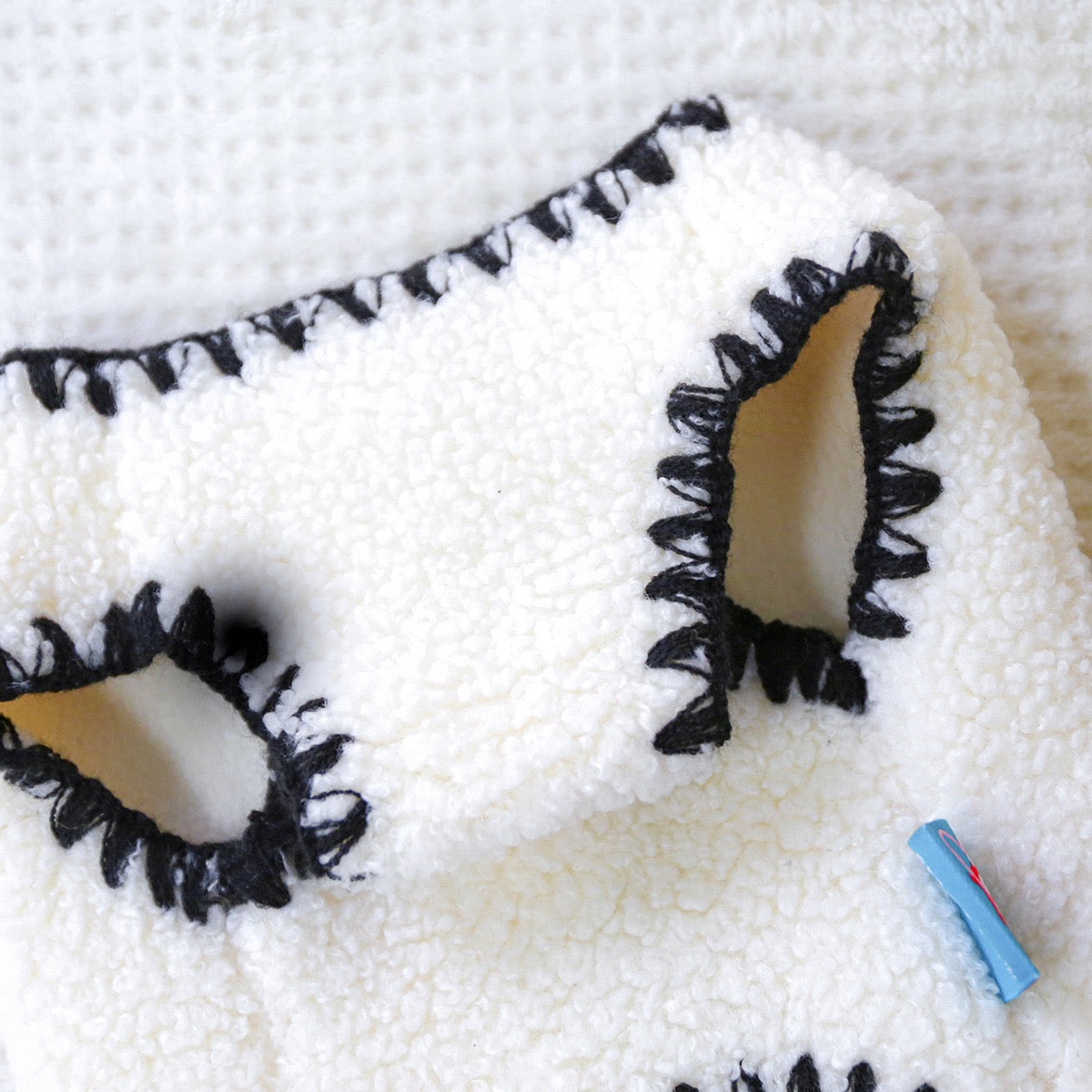 Macro shot of the bold black whipstitch edging on the white fleece. High-end tailoring that adds a structured, designer silhouette to the pet garment.
