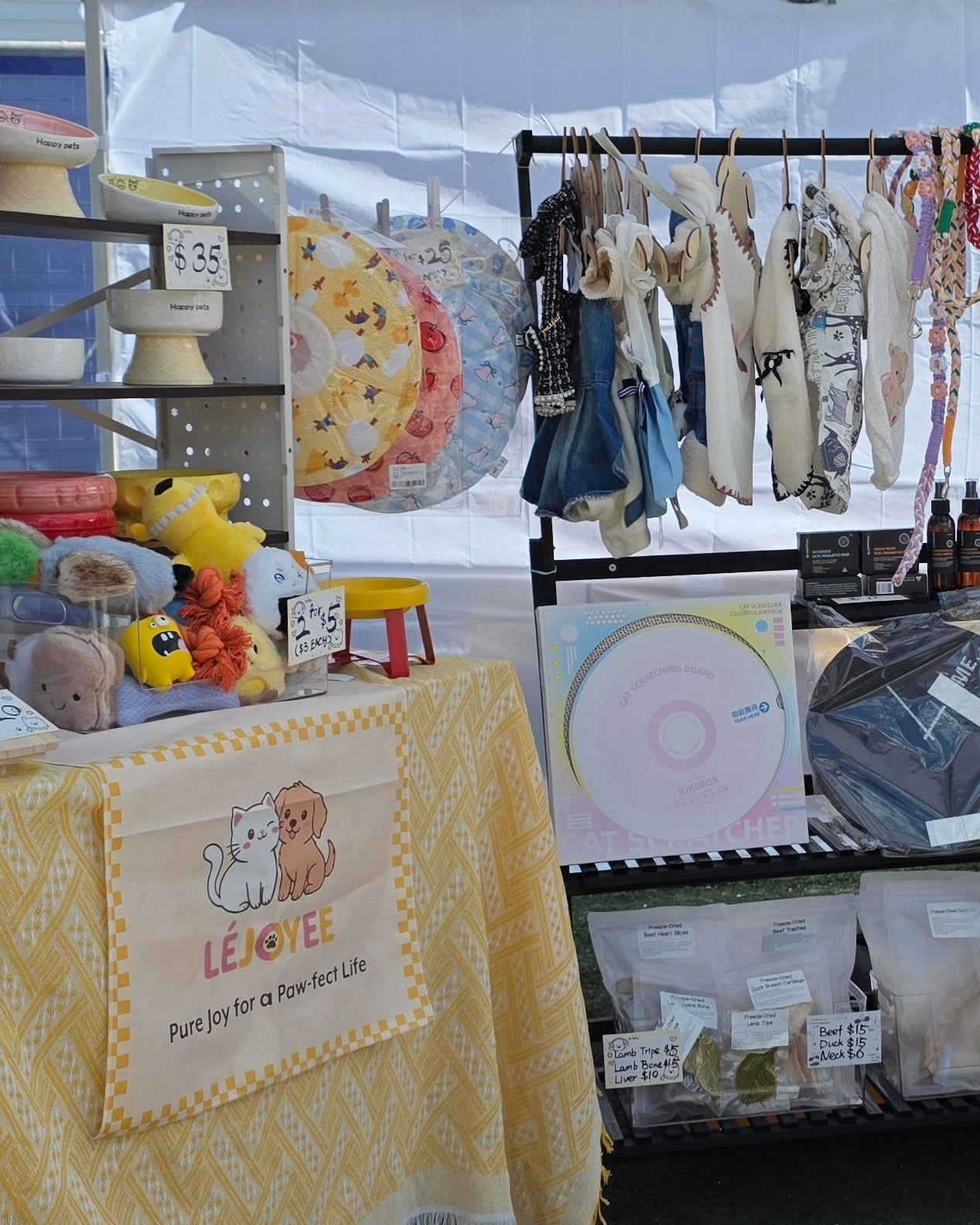 Stall with yellow tablecloths and various pet items on display under a white tent.