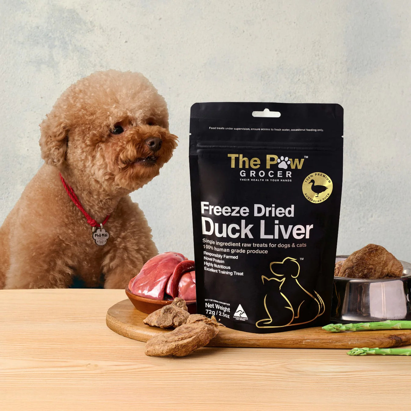 A cute poodle dog eagerly waiting for a high-value, hypoallergenic reward of The Paw Grocer Freeze-Dried Duck Liver, displayed next to fresh raw organ meat.