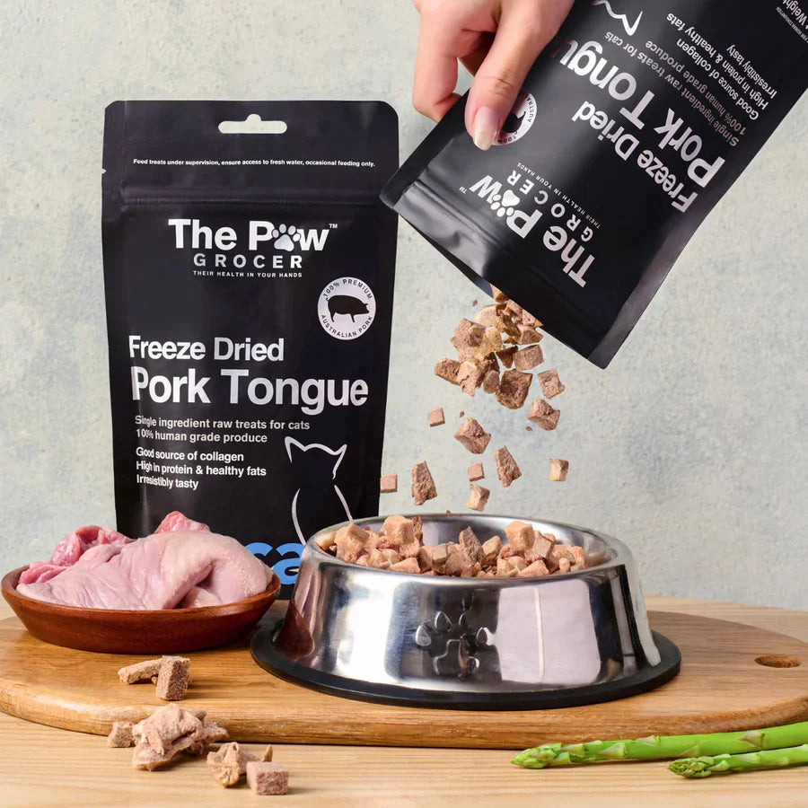 A hand pouring 100% pure freeze-dried pork tongue treats from the pouch into a silver pet bowl, showcasing the raw, crunchy cubed texture that acts as a flavor-boosting meal topper.
