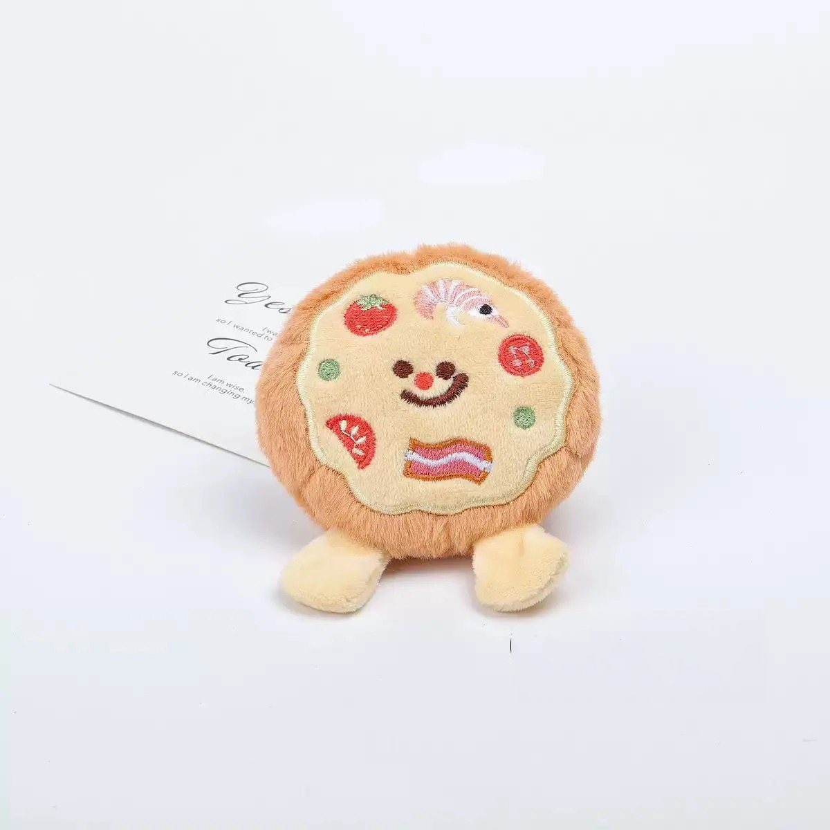 A round plush pizza toy featuring detailed embroidery of shrimp, tomatoes, and bacon, with a built-in squeaker.