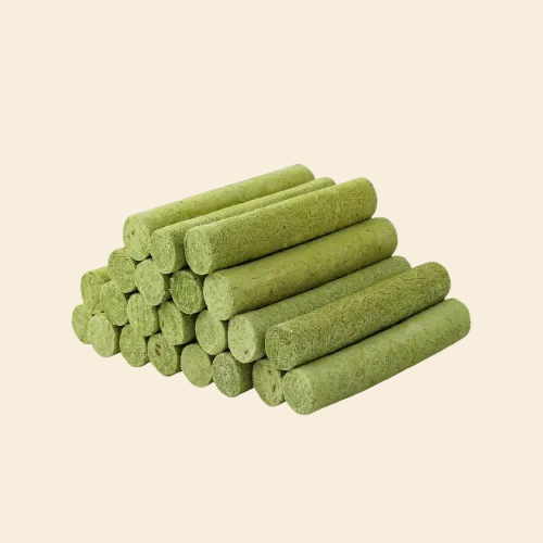 A neat pyramid stack of cylindrical green freeze-dried cat grass sticks on a light background, highlighting the visible natural grass fibers that safely stimulate digestion and provide hairball relief.