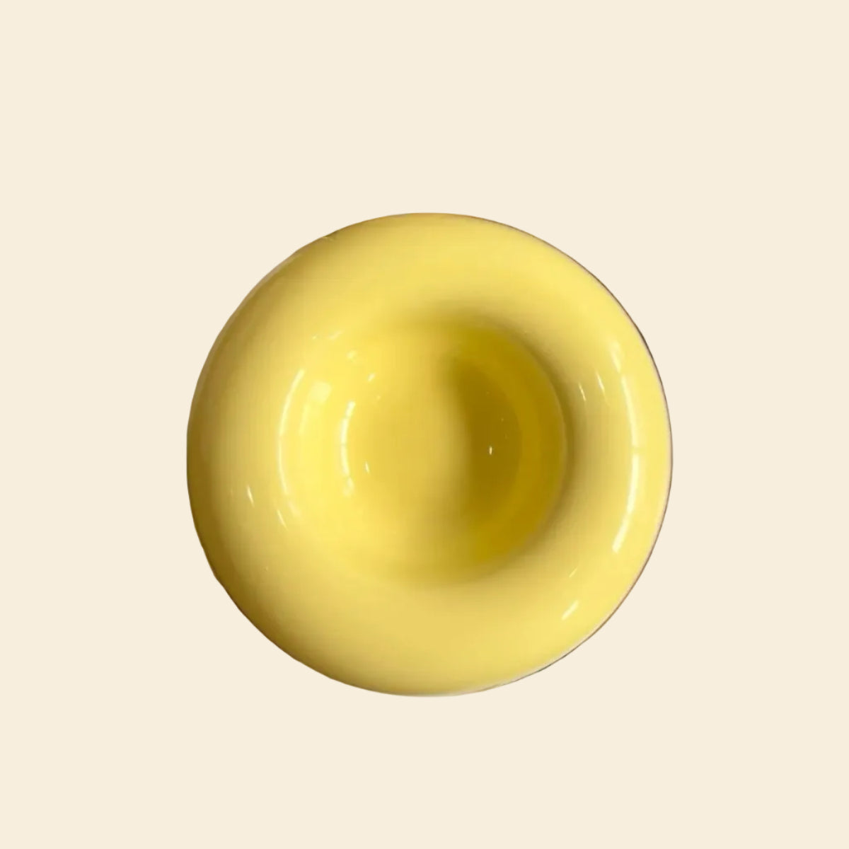 Top-down view of a Sunshine Yellow ceramic bagel pet bowl resting on an art book, showcasing its perfectly circular 80ml center capacity and vibrant glossy finish.