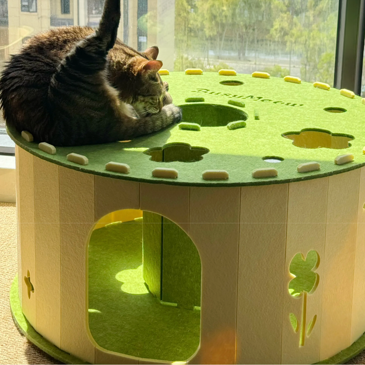 Cat lounging on a green and beige cat house with clover designs.
