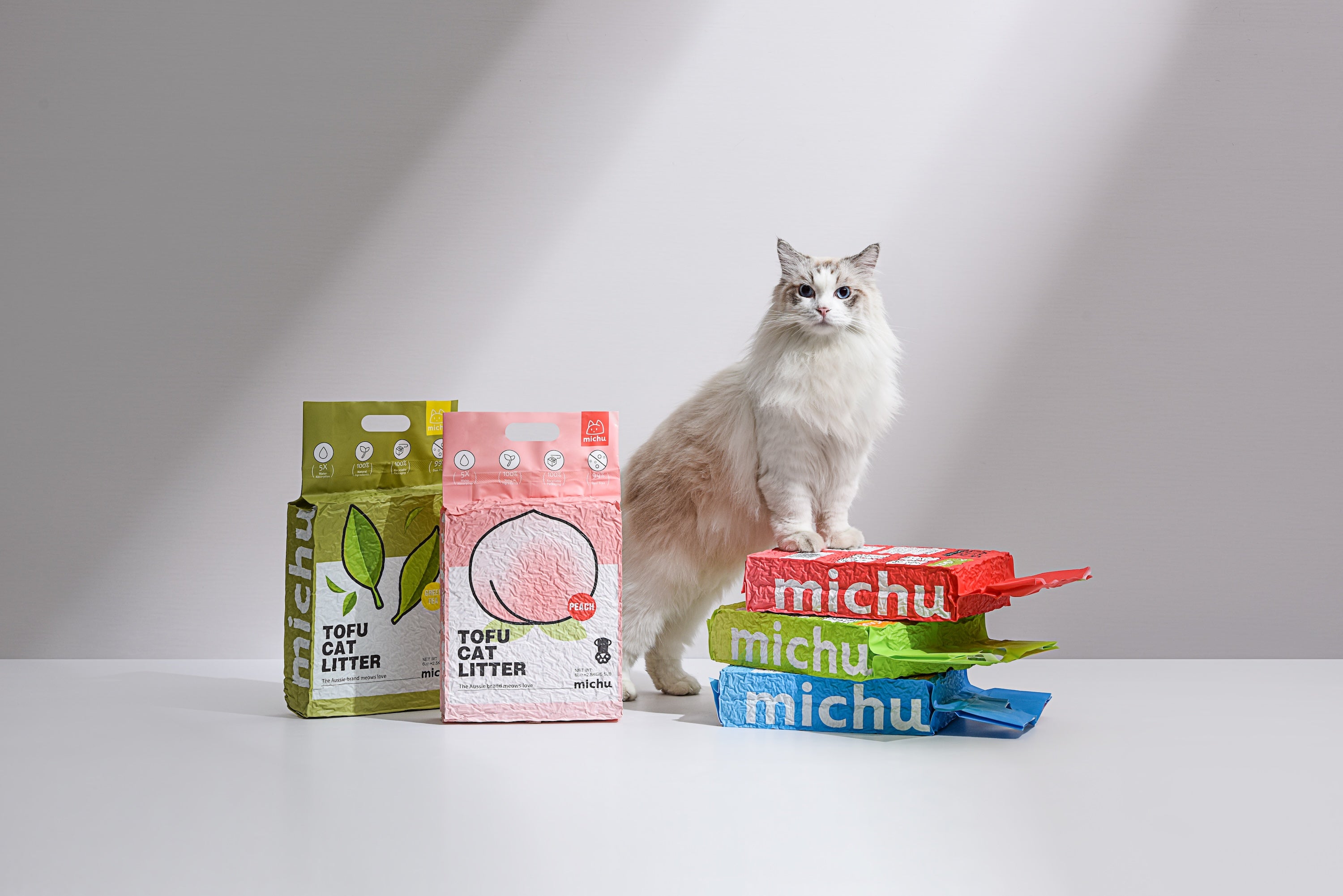 Cat sitting on a stack of Michu cat litter bags with other packages in the background.