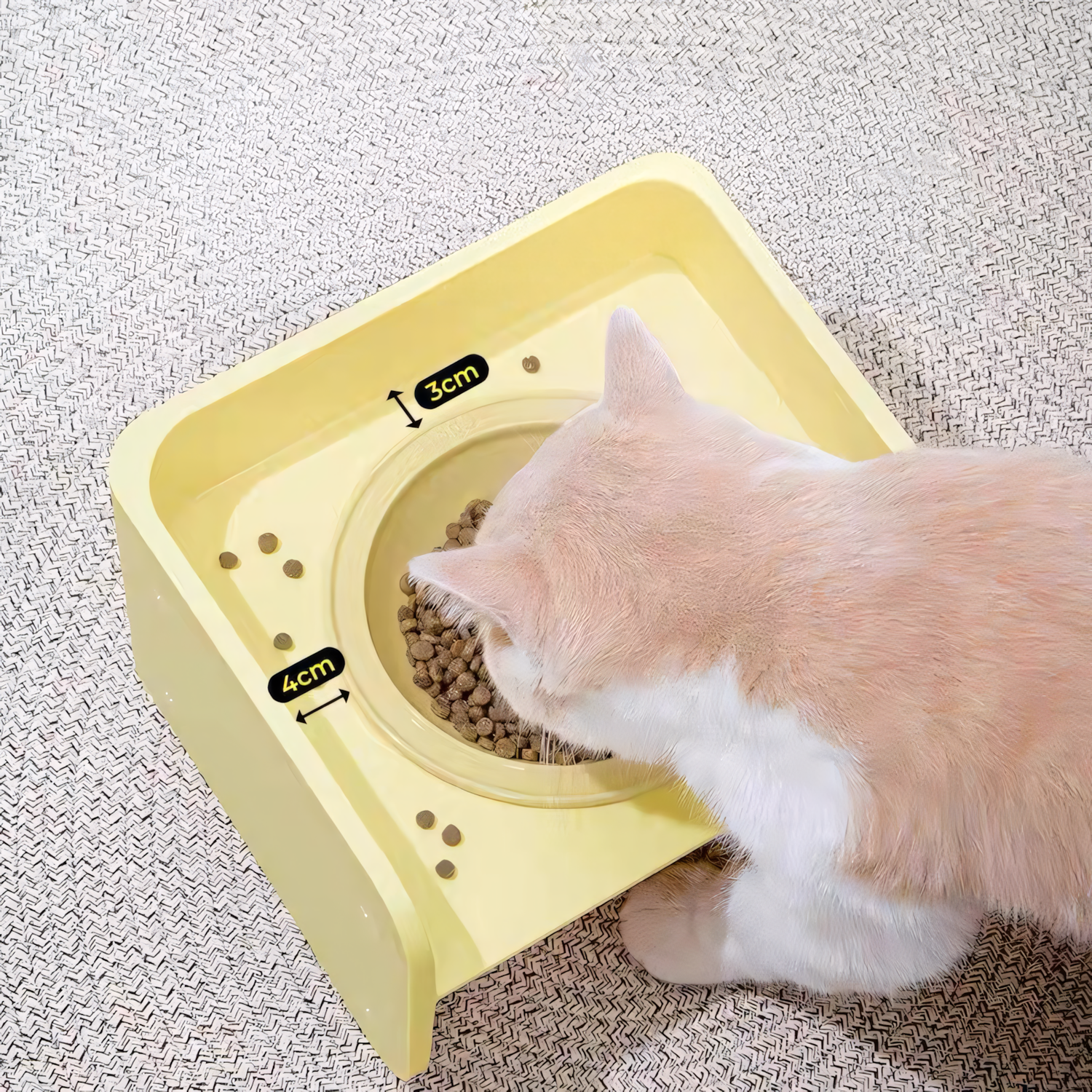 A white and orange cat eating kibble from the yellow Mango Square Table pet bowl. Graphics highlight the 3cm and 4cm extended guard margins designed to catch dropped food.