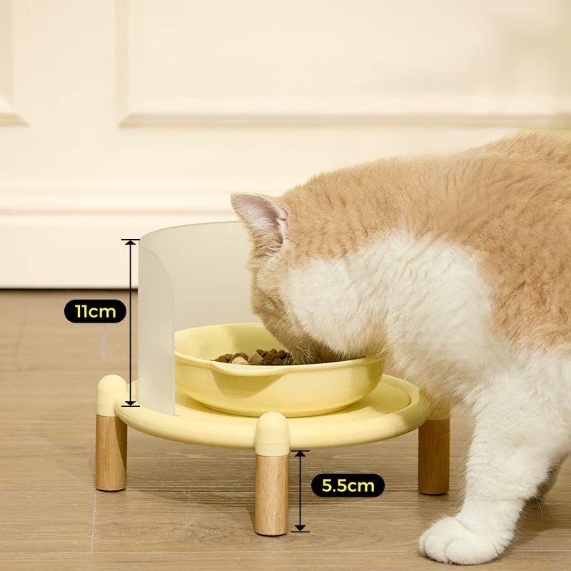 Side view of a cat using the Mango Elevated Feeder. Labels show the 5.5cm wooden legs for orthopedic support and the 11cm high splash guard to keep floors clean.