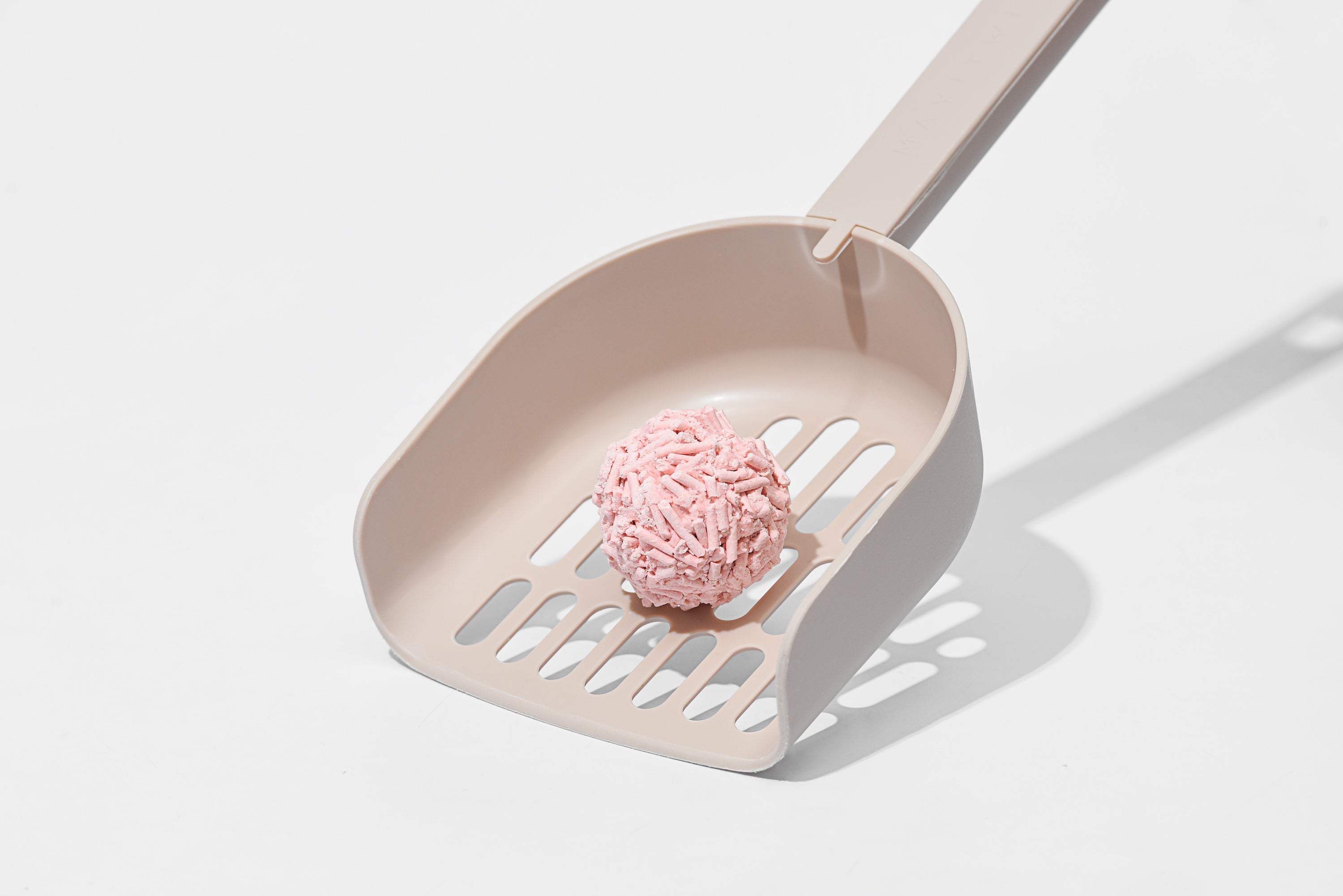 Pink cat litter scoop with a scoop of pink cat litter on a light gray background