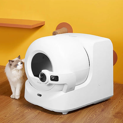 White self-cleaning litter box with a cat on a wooden floor against a yellow wall.