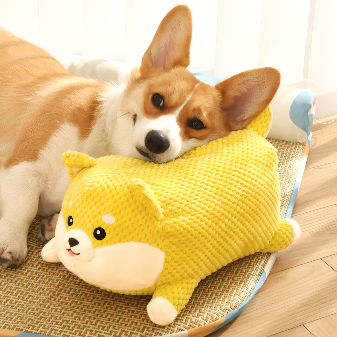 Corgi dog lying next to a yellow plush toy shaped like a dog on a wooden floor.