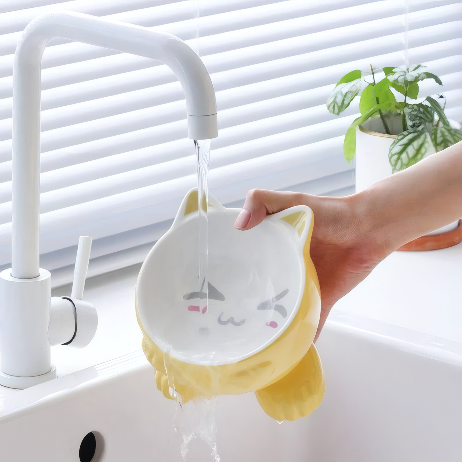 Yellow and white pet bowl with cat design being rinsed under a faucet.
