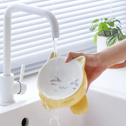 Yellow and white pet bowl with cat design being rinsed under a faucet.