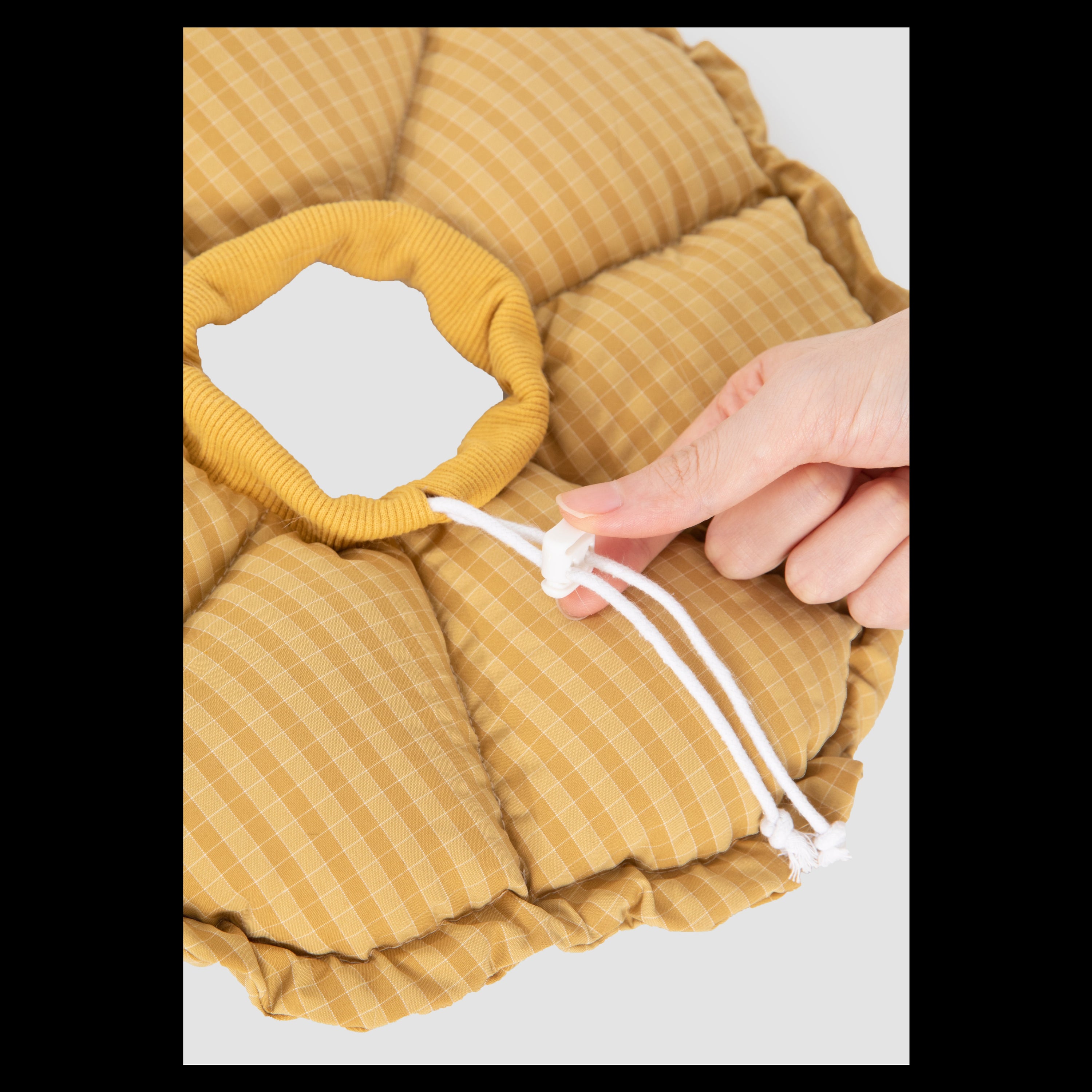 Close-up of a hand adjusting the toggle drawstring on the yellow gingham HiDREAM plush pet cone, showing the soft, ribbed inner neckband.