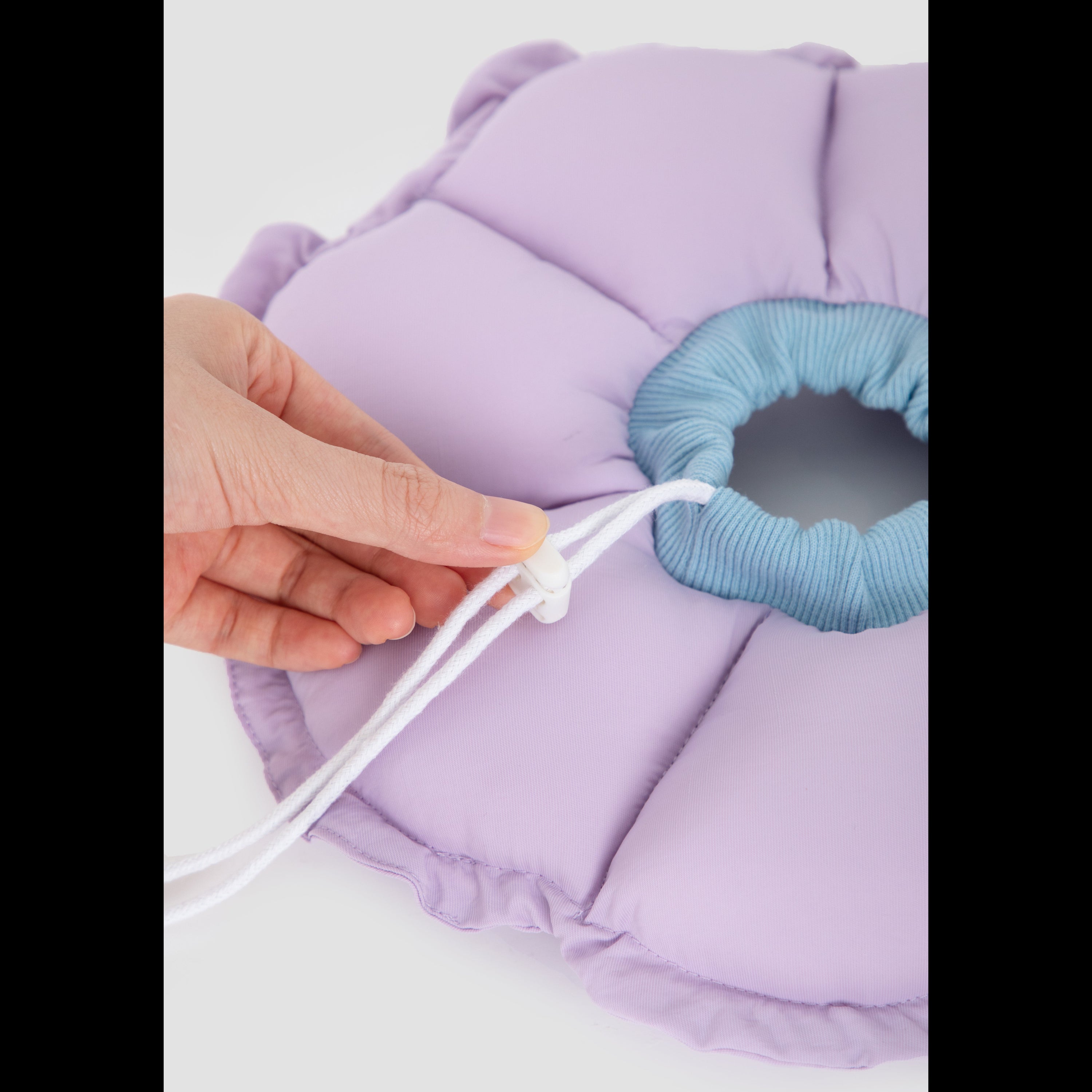 Close-up of a hand adjusting the customizable toggle drawstring on the purple HiDREAM plush recovery collar to ensure a secure, escape-proof fit.