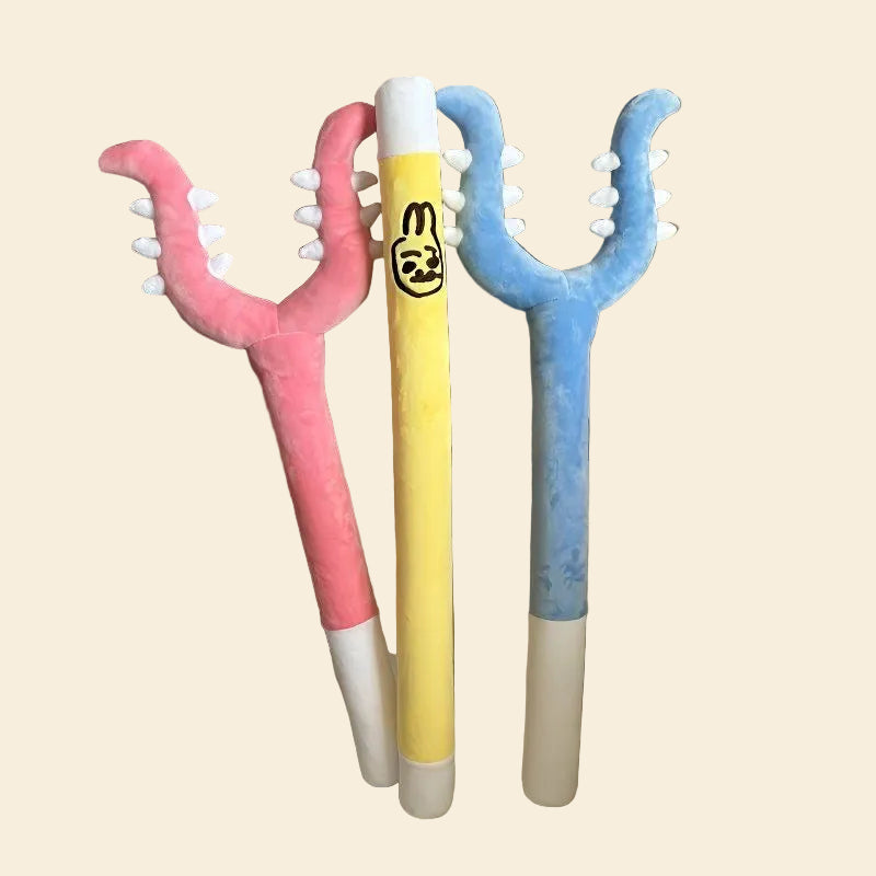 A collection of three oversized anime-inspired plush kicker toys, including a pink defender fork, a yellow rabbit wand, and a blue defender fork, resting together on a white chair.