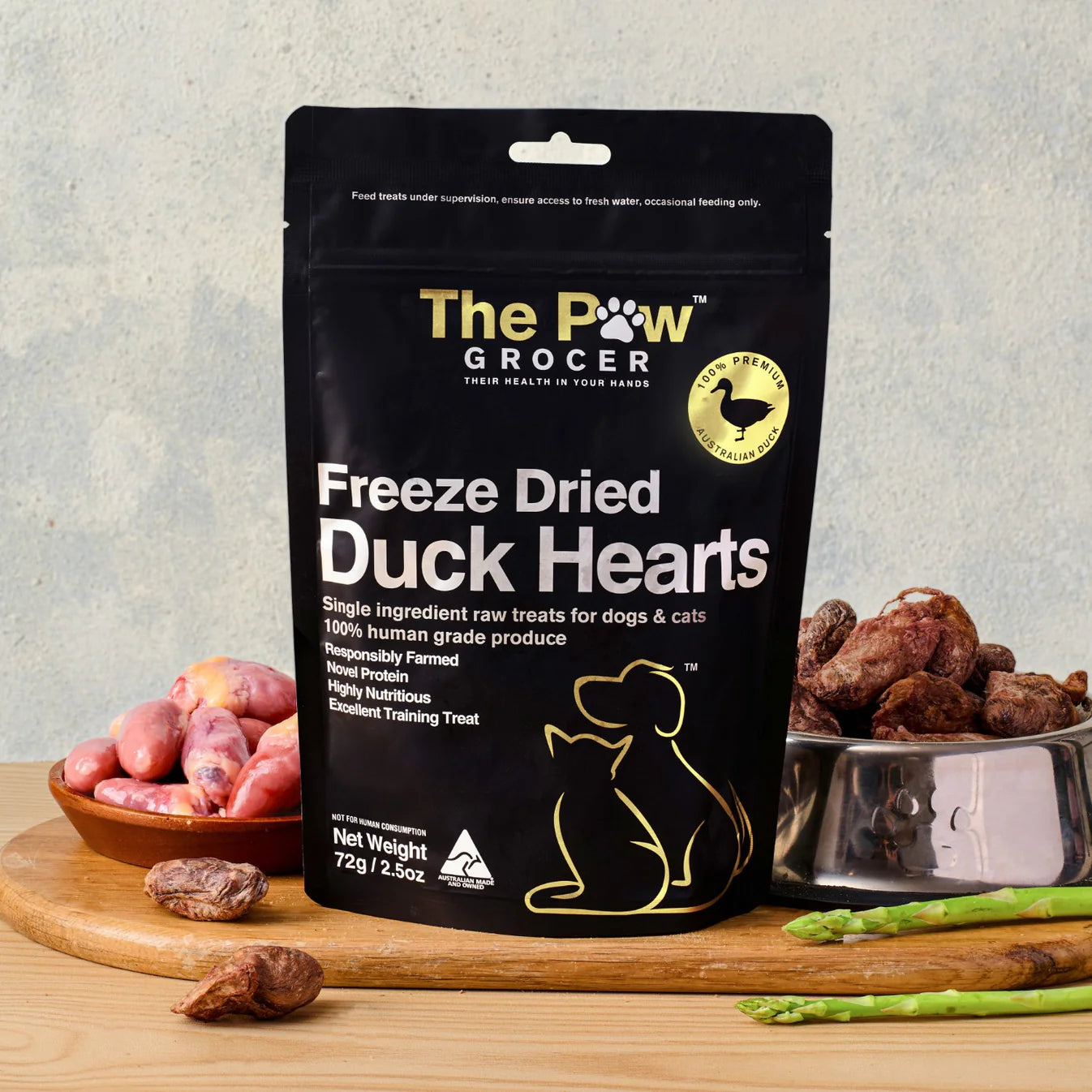 The Paw Grocer 72g Freeze-Dried Duck Hearts treats perfectly displayed on a wooden board next to fresh raw duck hearts and a silver bowl filled with the zero-carb, hypoallergenic reward.