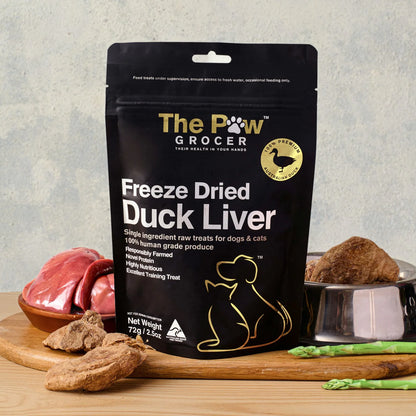 The Paw Grocer 72g Freeze-Dried Duck Liver treats displayed on a wooden board next to fresh raw duck liver and a silver bowl filled with the vitamin-packed, hypoallergenic cubes.