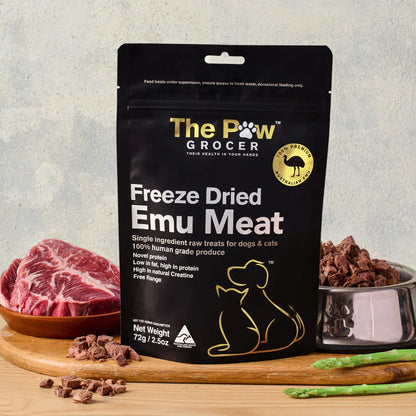 The Paw Grocer 72g Freeze-Dried Emu Meat treats displayed on a wooden board next to a cut of fresh raw meat and a silver bowl filled with the crunchy, hypoallergenic cubes.