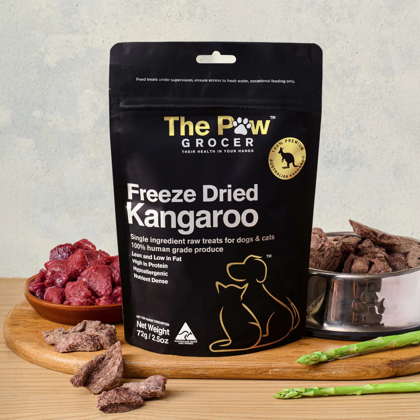 The Paw Grocer 72g Freeze-Dried Kangaroo pet treats displayed on a wooden board next to fresh raw meat and a silver bowl filled with the crunchy, hypoallergenic cubes.