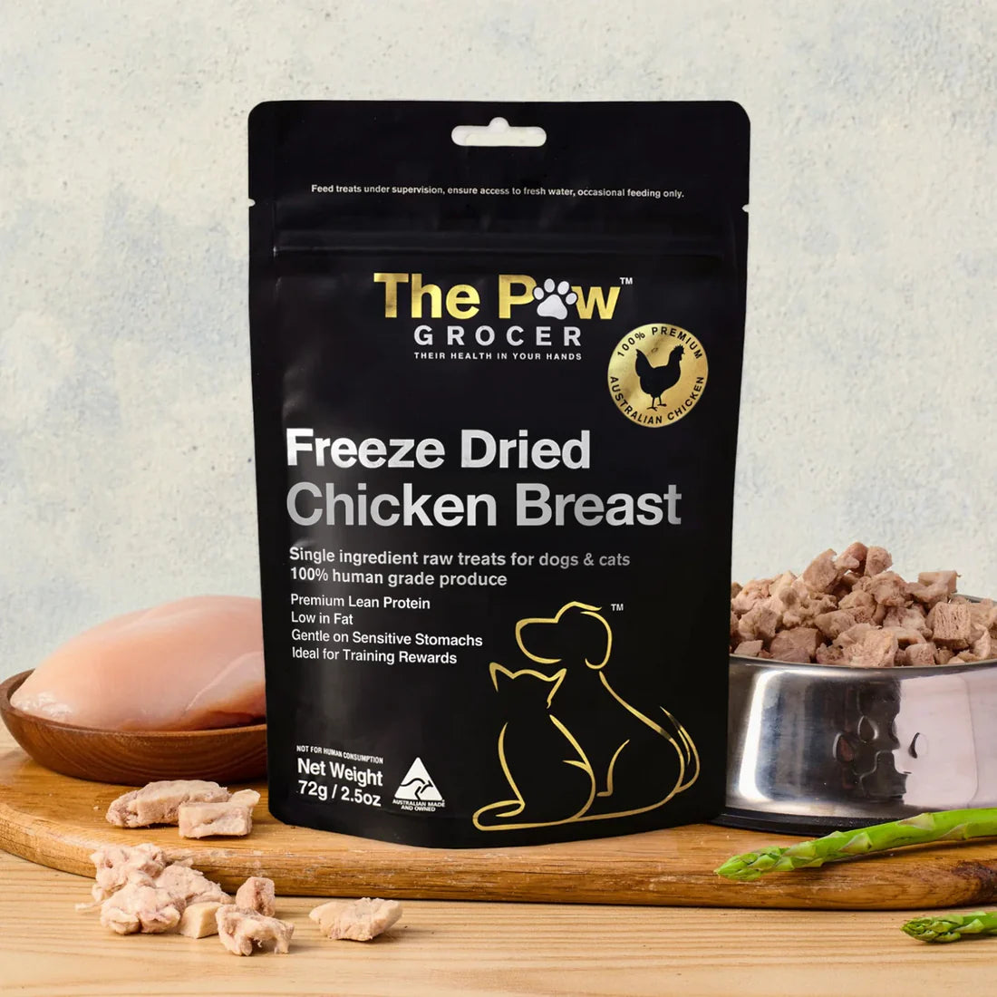 The Paw Grocer 72g Freeze-Dried Chicken Breast treats beautifully displayed on a wooden board next to fresh raw meat and a silver bowl filled with the highly digestible, guilt-free reward.