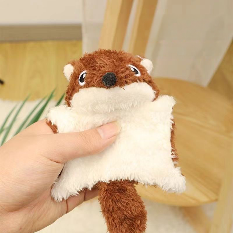 A hand holding a soft brown and white plush flying squirrel pet toy, highlighting its flat design and ultra-soft texture that is gentle on teeth and gums.