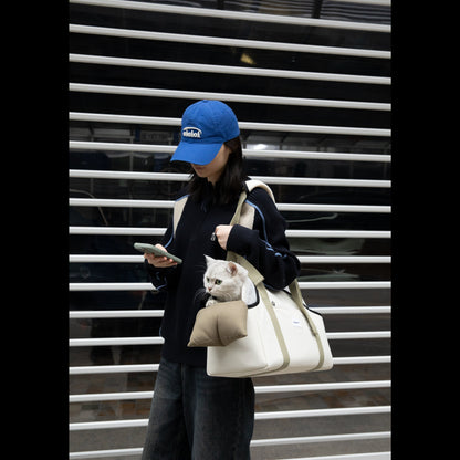 A pet owner carrying the canvas-style cat tote bag on her shoulder. A silver cat is safely looking out from the U-shaped opening while resting on the built-in chin pad.