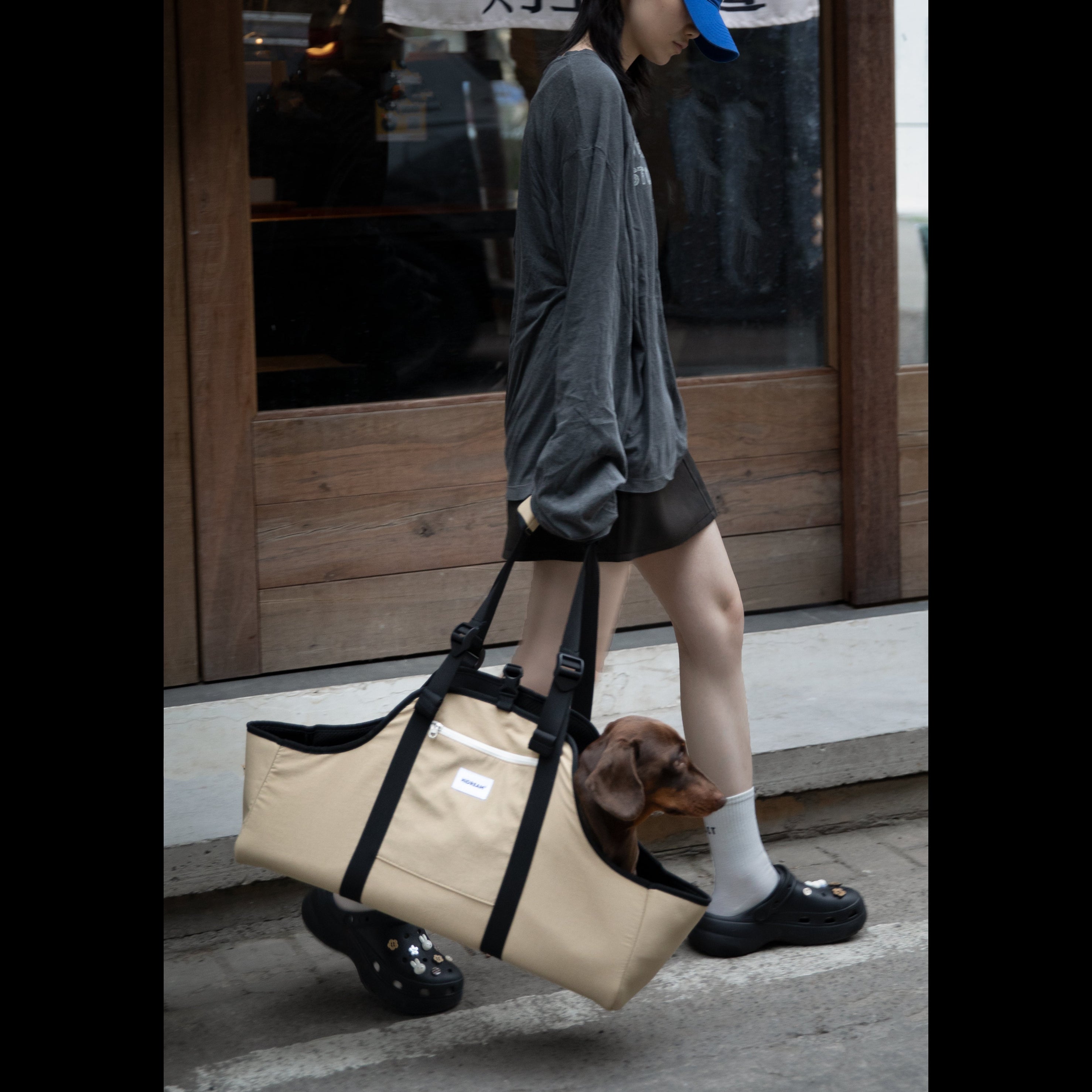 Lifestyle shot of a person walking outdoors with the Clay Brown Sausage Dog Carrier Tote, demonstrating its style and portability for travel.