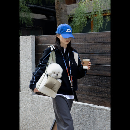 A pet parent walking through the city wearing the crossbody pet carrier, with a small fluffy white dog comfortably resting its chin on the ergonomic side pillow.