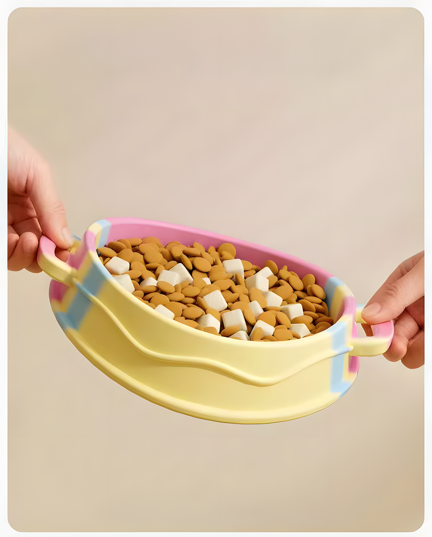 A pair of hands easily carrying the pastel swirl silicone slow feeder bowl filled with dry kibble, highlighting the convenient double handles that keep hands clean.