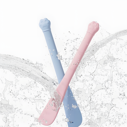 Blue and pink silicone cat food spatulas being splashed with water, demonstrating their water-resistant material and effortless cleaning process.