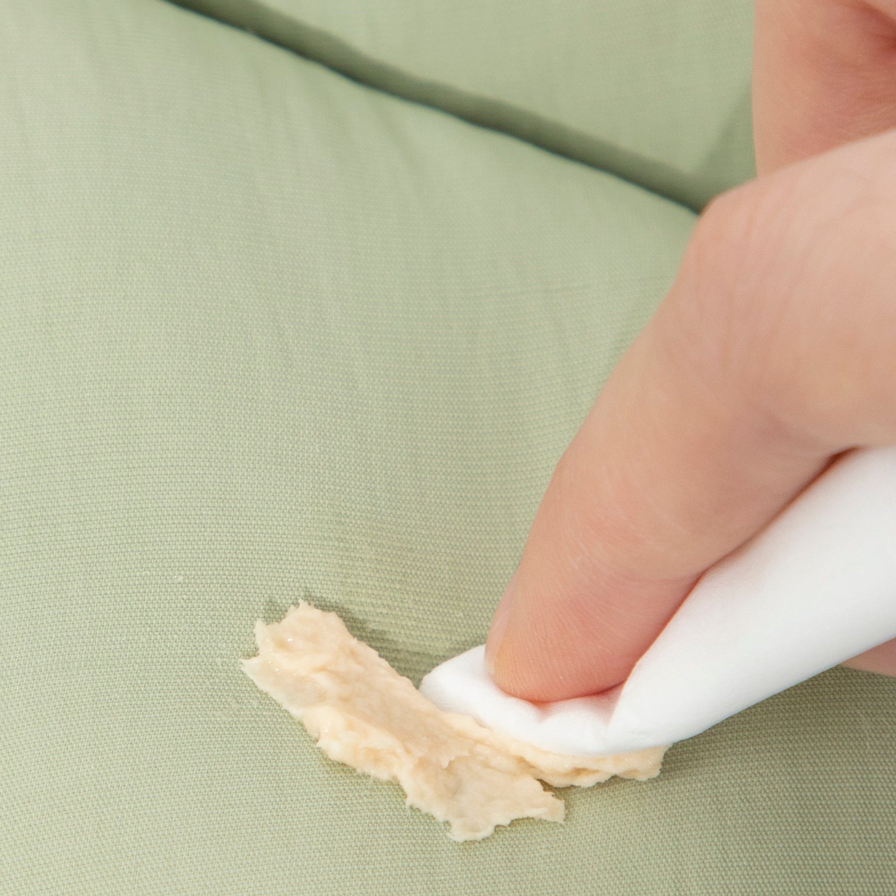 A hand easily wiping a food stain off the dirt-resistant, water-repellent fabric of the green HiDREAM soft pet recovery collar.