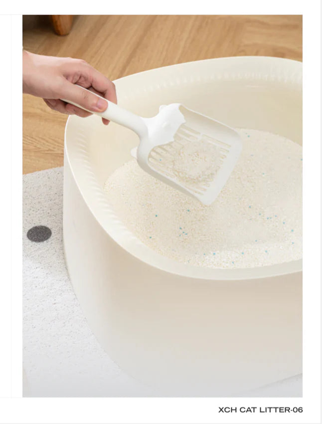 A hand using a white scoop to effortlessly lift a firm, round clump of Xu Cuihua natural cassava cat litter from a white litter box, showcasing its rapid clumping performance and fine, paw-friendly texture with visible blue silver ion granules.