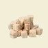 A close-up view of premium freeze-dried cod cubes piled on a light blue background, highlighting the single-ingredient, ultra-high protein ocean treat for pets.