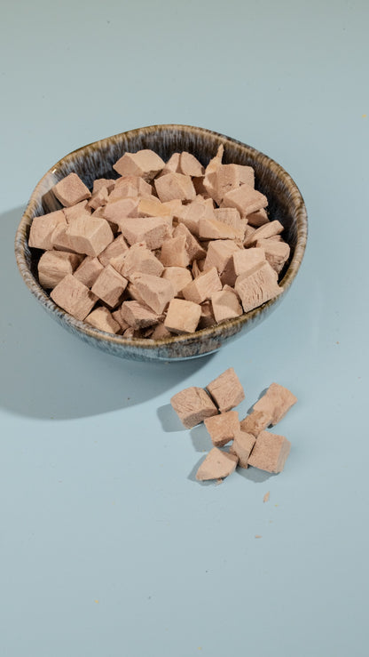Bowl of freeze-dried duck cubes c on a light blue background
