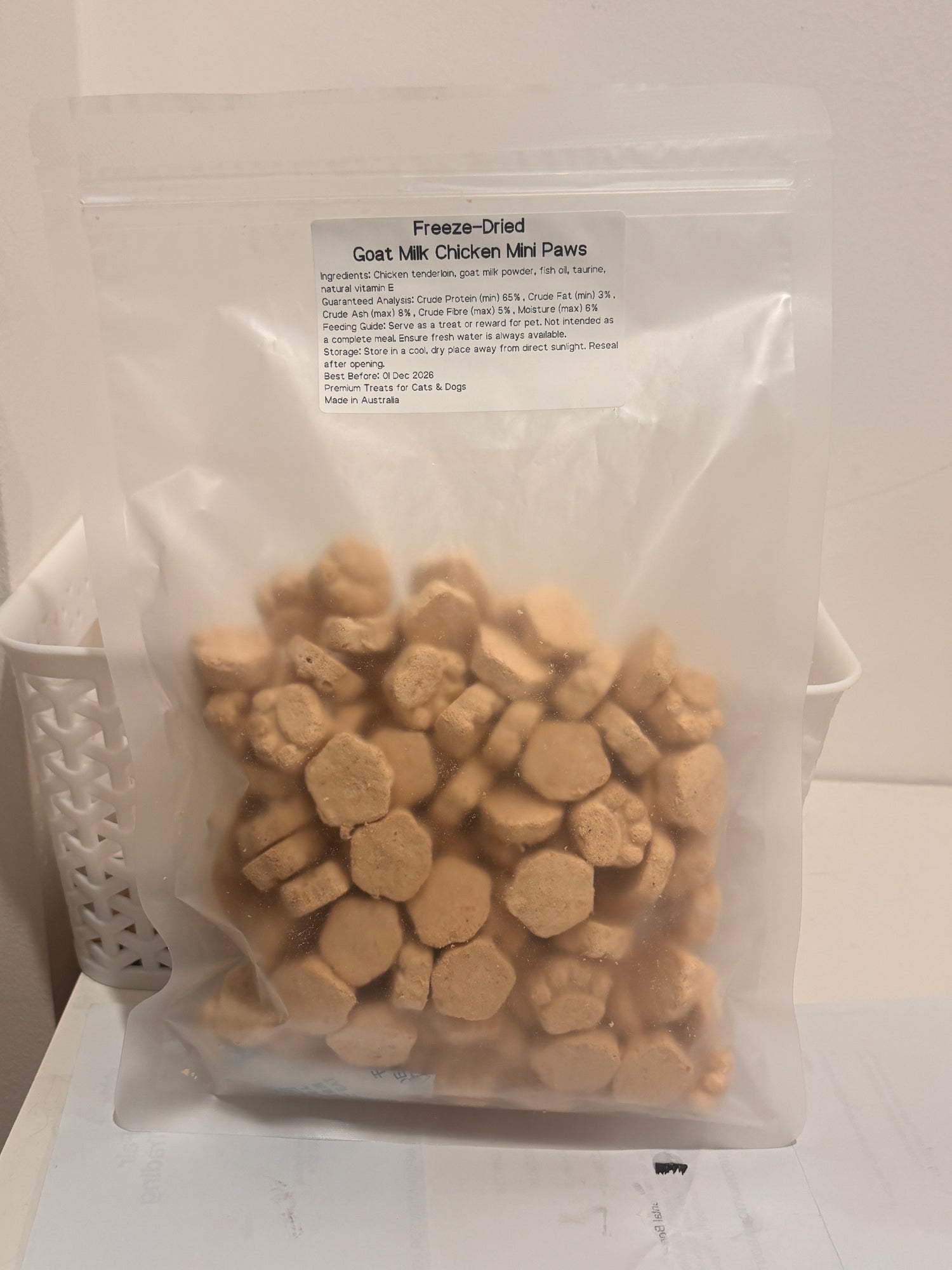 A clear, resealable bag of Freeze-Dried Goat Milk Chicken Mini Paws pet treats, showing the printed label with ingredients like chicken tenderloin, goat milk powder, and fish oil, while highlighting that it is Made in Australia.