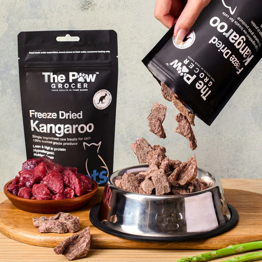 Hand pouring freeze-dried kangaroo cubes into a cat bowl. Showcasing the real meat texture used as a high-value reward or meal topper for picky cats.