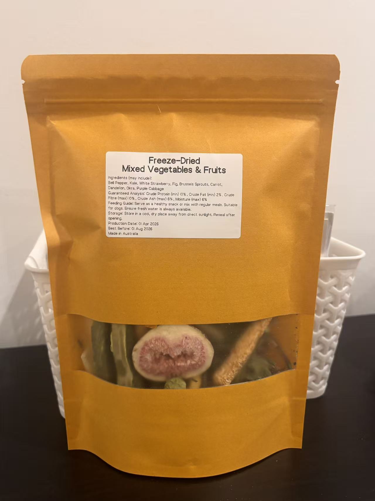 A real-world photo of the Freeze-Dried Mixed Vegetables &amp; Fruits dog treat in a premium kraft pouch. The label displays the Australian-made origin and ingredients, with a clear window showing a freeze-dried fig slice and healthy green veggies.