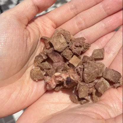 A person holding a handful of diced freeze-dried raw lamb hearts. Showcasing the perfectly small diced size ideal for cat and dog training, enrichment toys, and meal toppers.