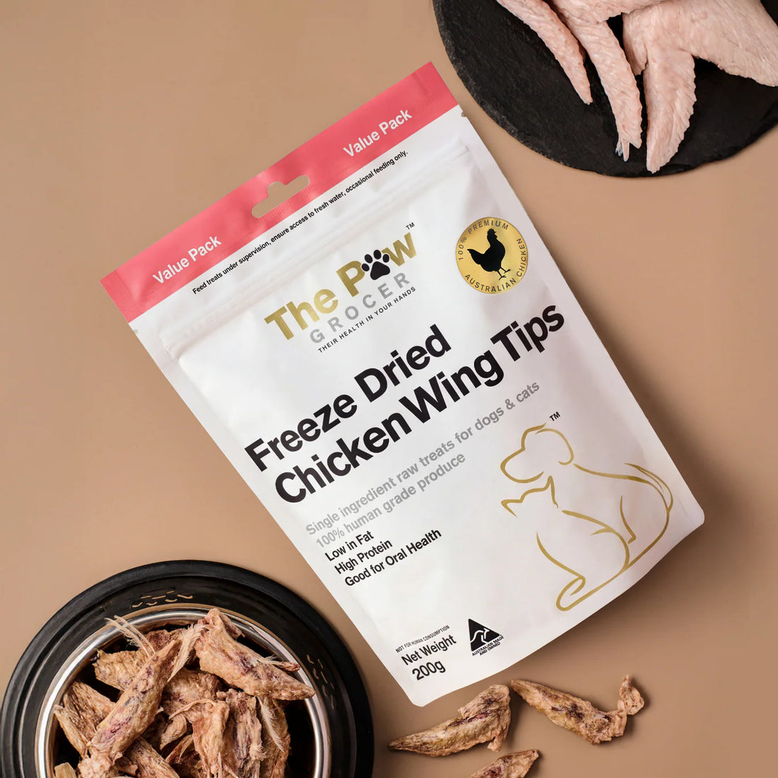 A value pack bag of The Paw Grocer Chicken Wing Tips next to fresh raw chicken wings and a bowl of crunchy freeze-dried treats. Single ingredient raw treats for dogs and cats.