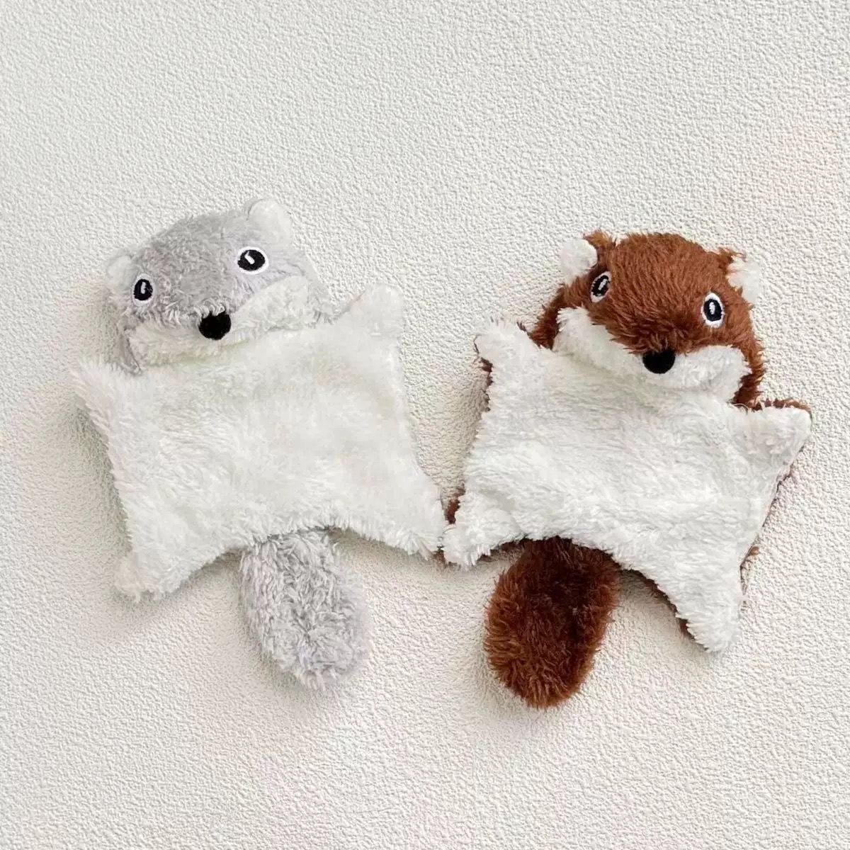 Two plush flying squirrel pet toys, one in grey and one in brown, lying flat side-by-side on a textured white surface to showcase the adorable woodland color options.