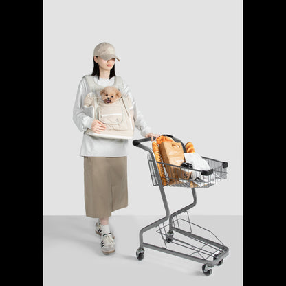 A woman easily pushing a grocery cart while comfortably carrying her small poodle in a beige, hands-free front pet carrier backpack.