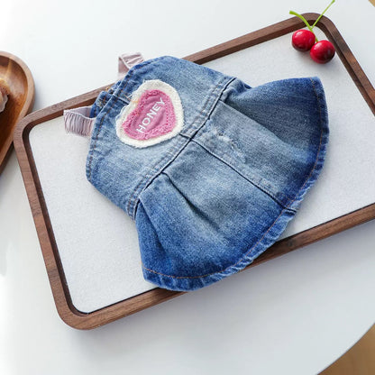 Flat lay of the Honey Heart Denim Dog Dress beautifully presented on a wooden tray, showing the vintage wash, pleated skirt, and pink heart applique.