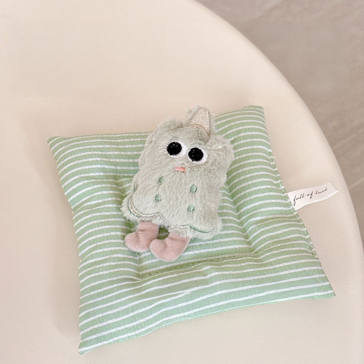 A close-up view of the kawaii green matcha biscuit plush squeaky toy, showcasing its soft texture, embroidered smiling face, and tiny decorative party hat.