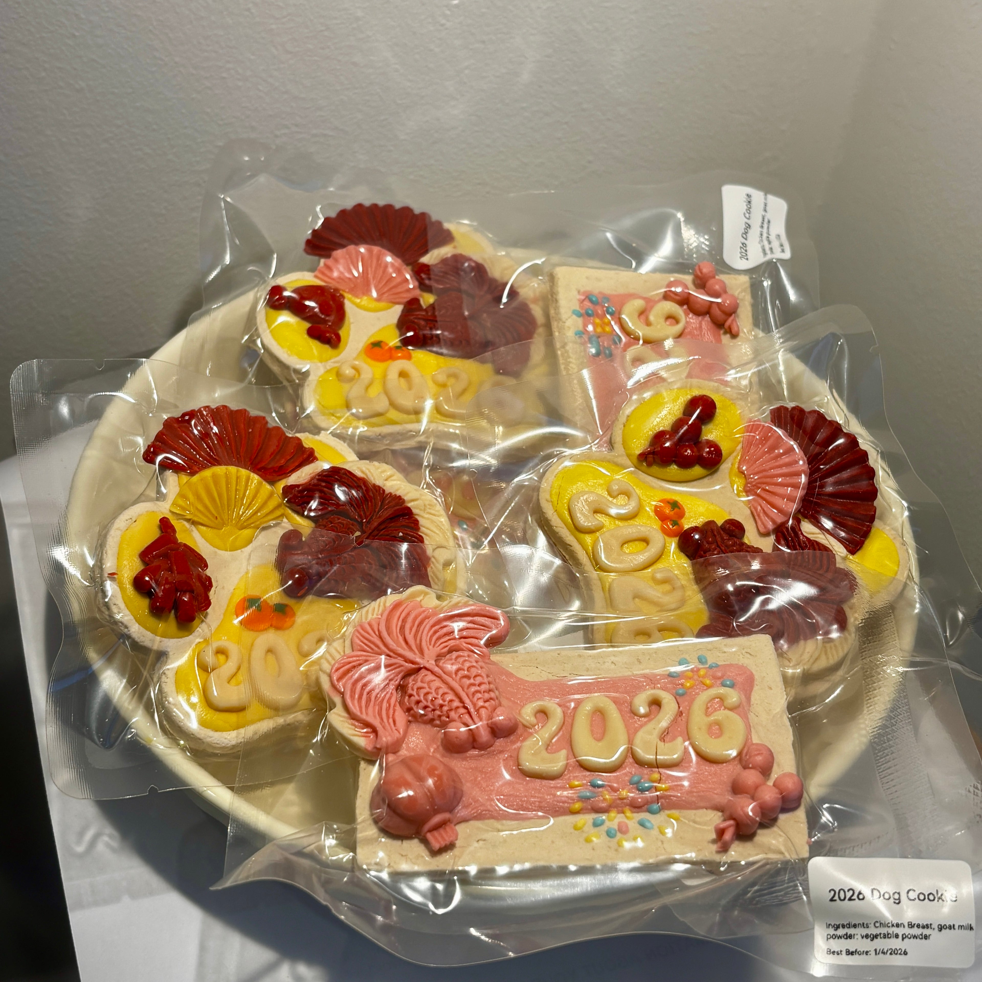 A collection of assorted 2026 New Year dog cookies on a plate, featuring "Lucky Paw" and "Festive Tablet" designs for dog holiday celebrations.